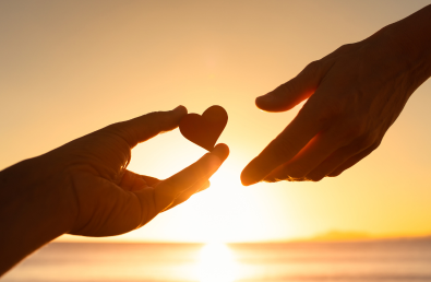 One hand holding a small heart and another reaching out with a sunset backdrop