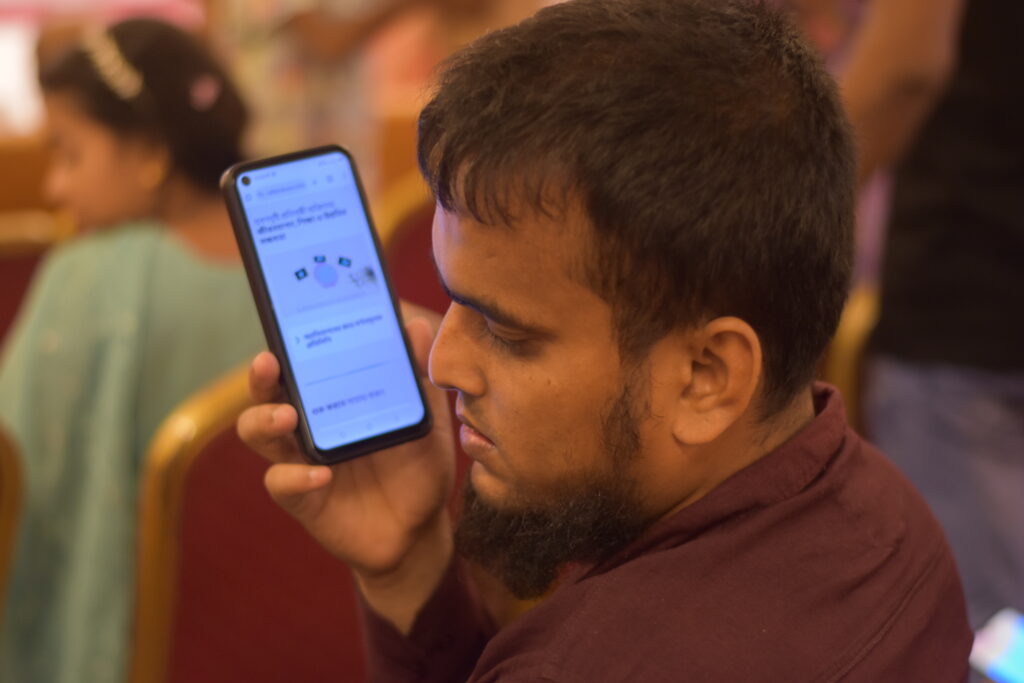  জুবায়ের তার কানের কাছে মোবাইল ফোন ধরে শ্রবণদৃষ্টি প্রতিবন্ধিতা বিষয়ক বৈশ্বিক রিসোর্স হাবে থাকা একটি রিসোর্স মনোযোগ দিয়ে শুনছে। 